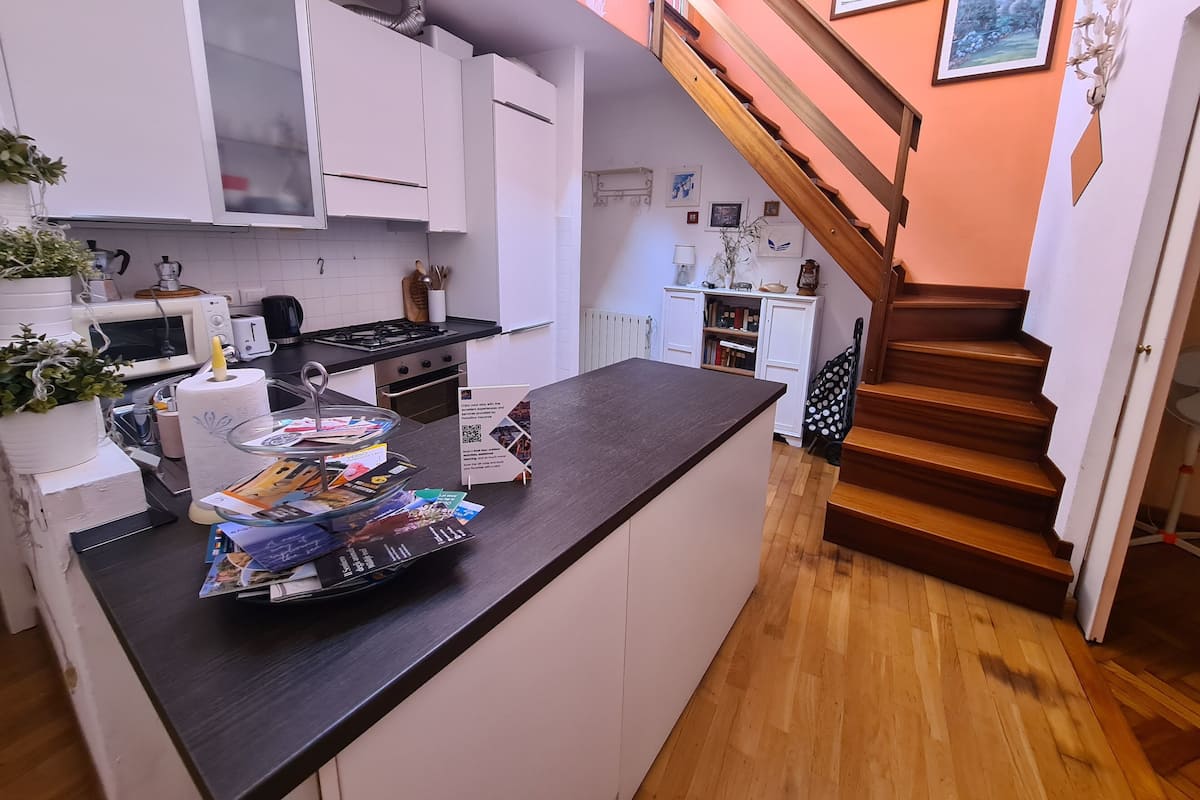 Een moderne keuken met witte kasten, een houten trap en een klein eiland met tijdschriften.