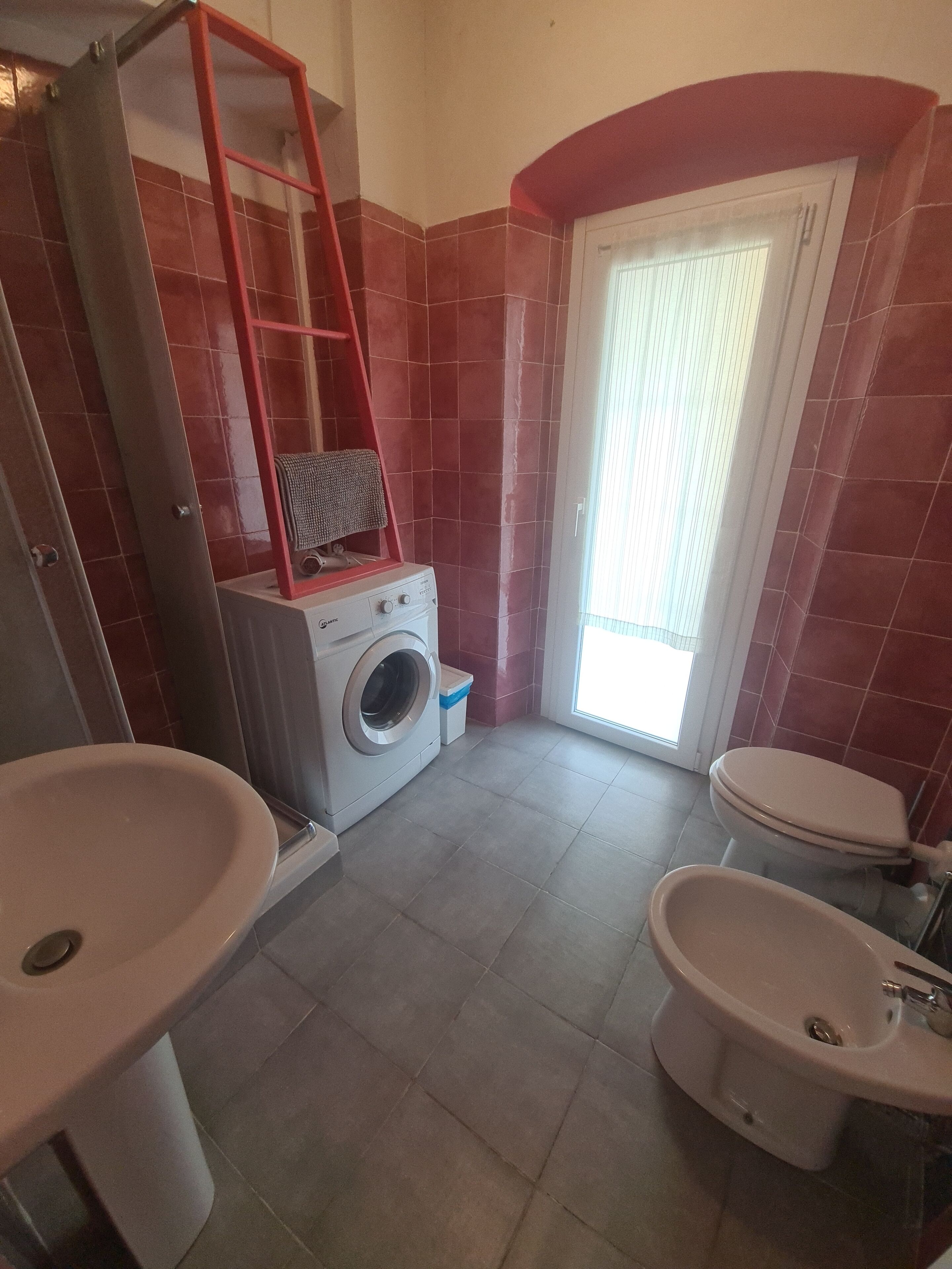 A bathroom with a washing machine, two sinks, a toilet, and a shower area.