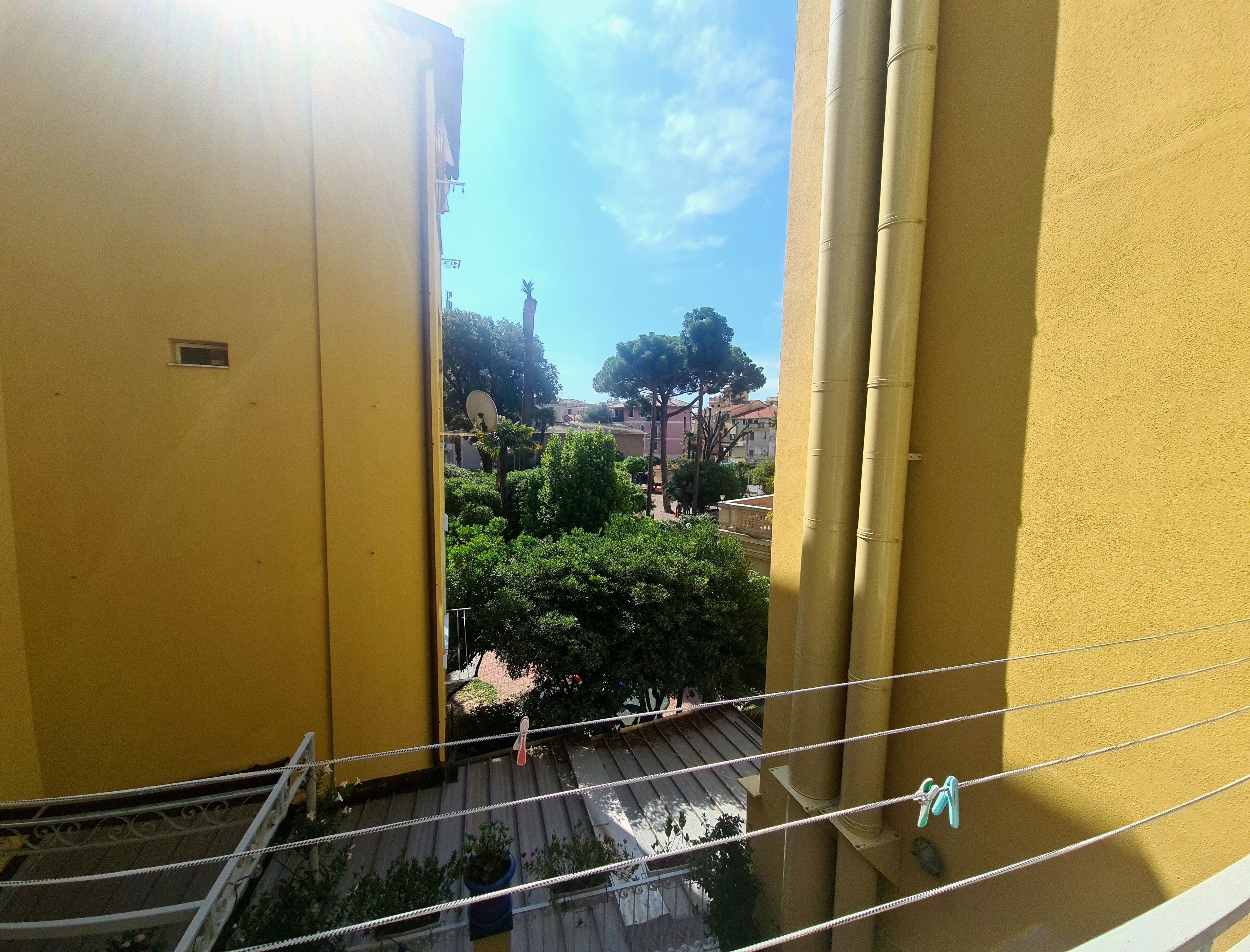 En gul bygning med balkon, der ud til en gårdhave med træer og en klar himmel.