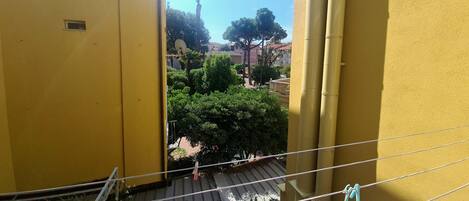 A yellow building with a balcony overlooking a courtyard with trees and a clear sky.