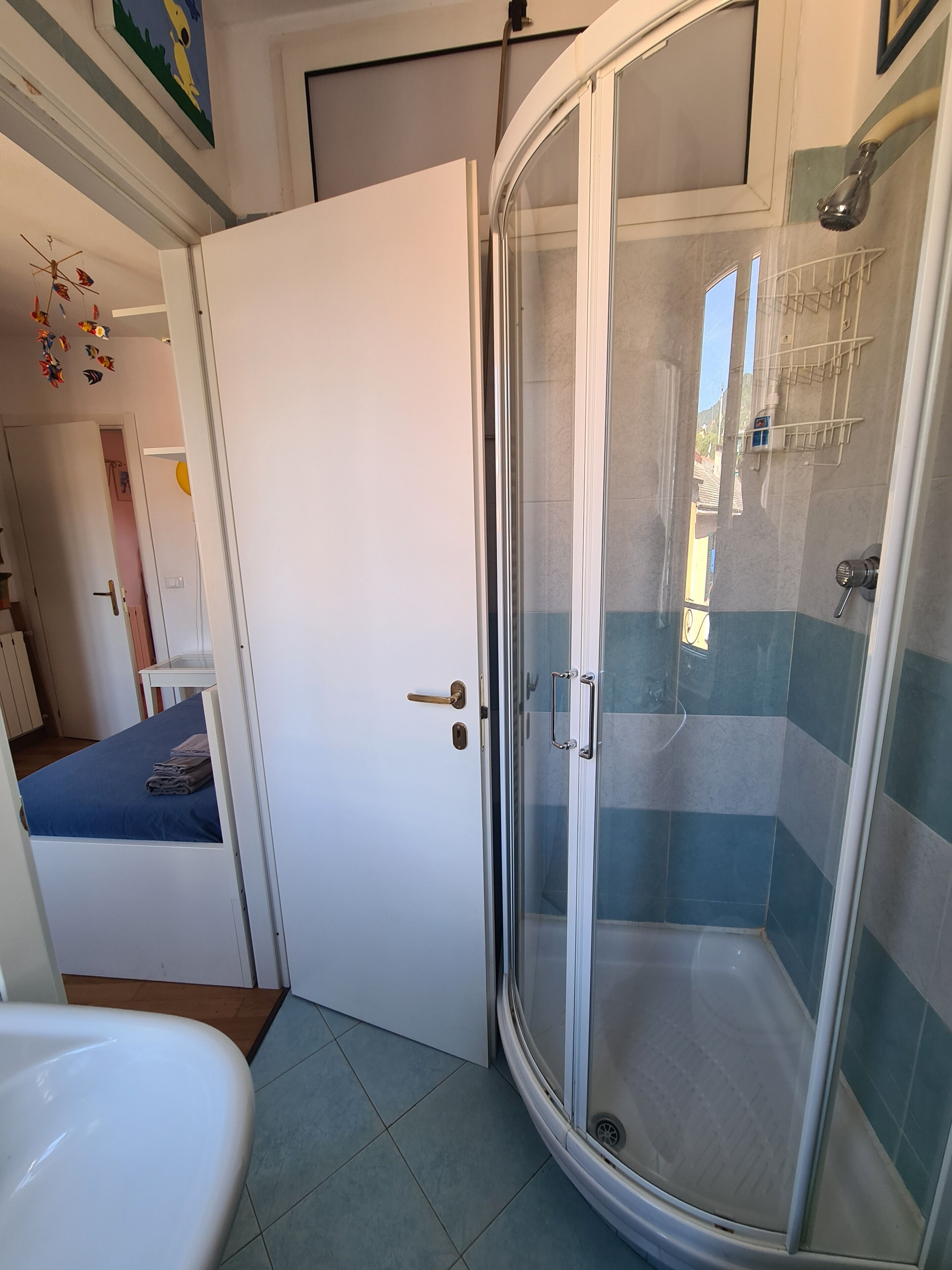 Ein Badezimmer mit einer Duschkabine, einem weißen Waschbecken und einem Bett mit blauer Bettwäsche.