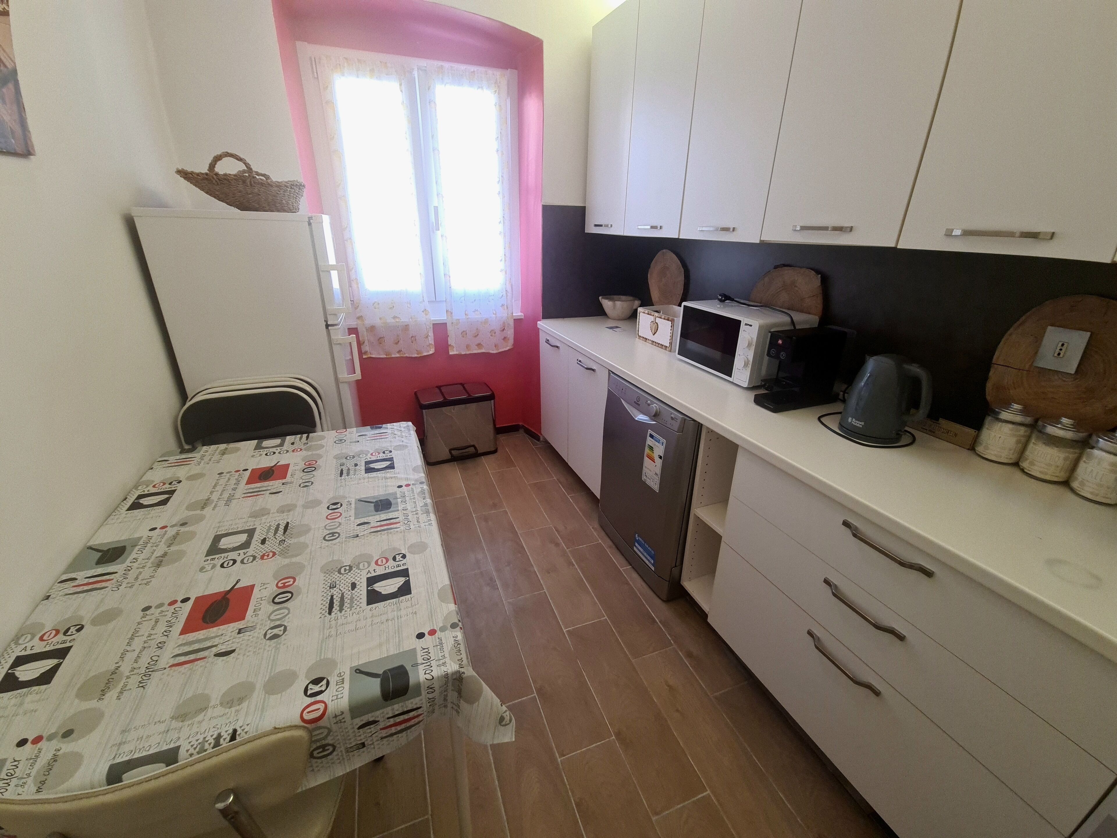A compact kitchen with a dining table, white cabinets, a microwave, and a kettle.