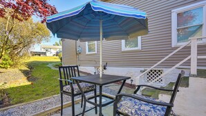 Un patio al aire libre con una mesa, sillas, un paraguas a rayas y una casa al fondo.