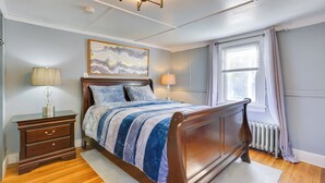 Un dormitorio con una cama de madera, una mesita de noche, una lámpara, un radiador y una ventana con cortinas.