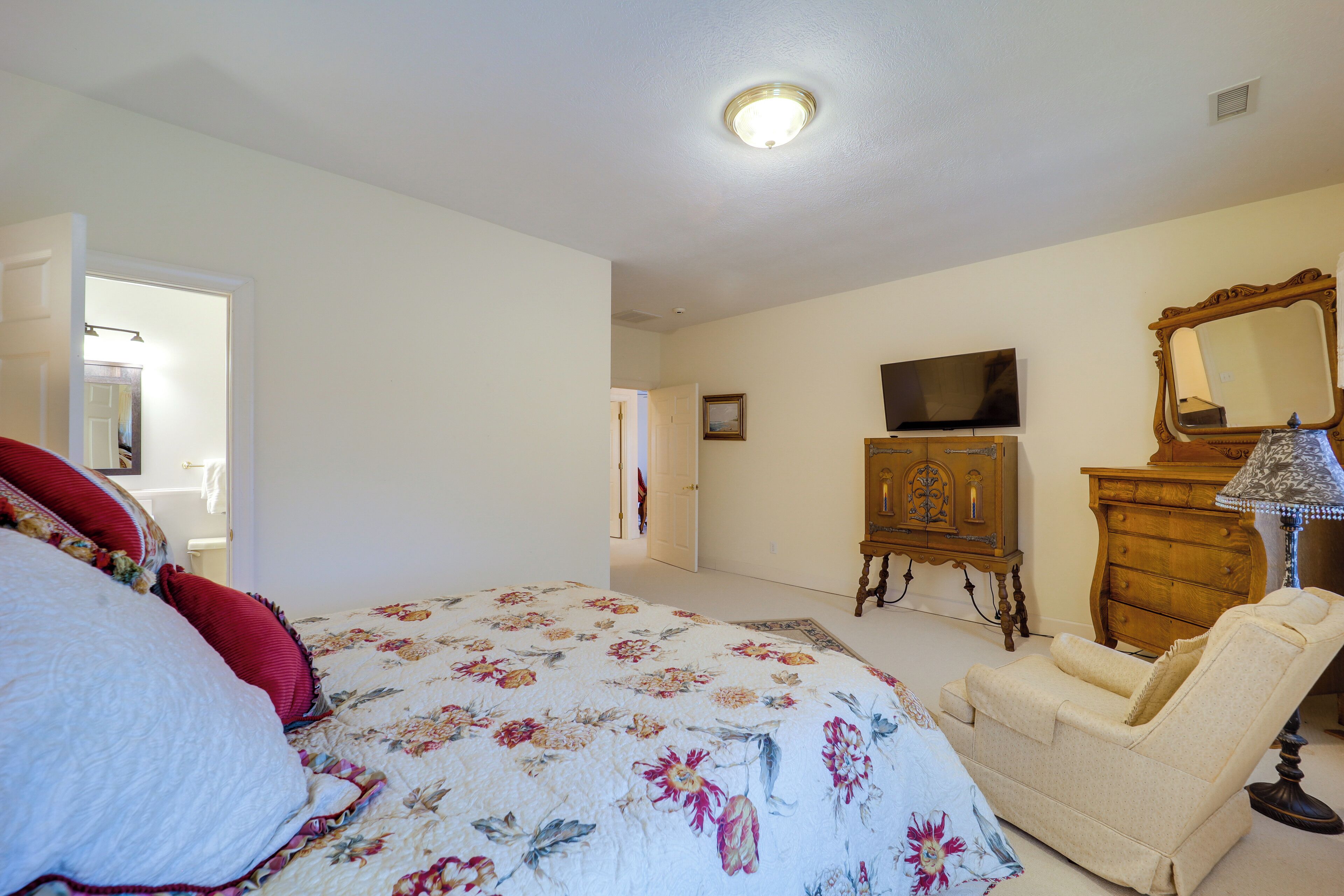 A bedroom with a bed, a chair, a dresser, a television, and a mirror.