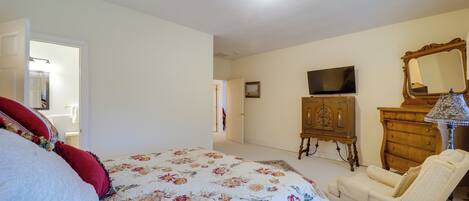 A bedroom with a bed, a chair, a dresser, a television, and a mirror.