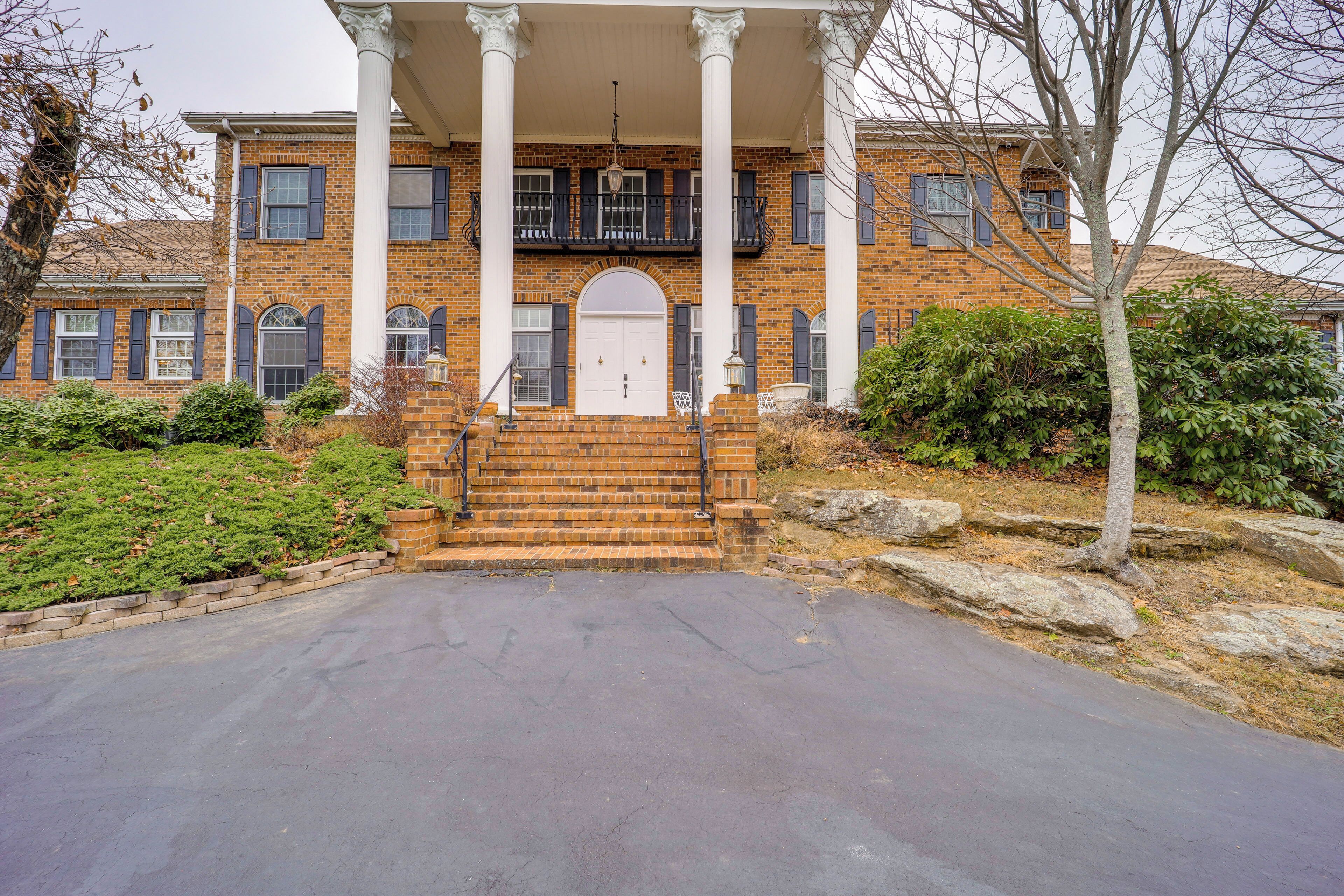 A two-story brick house with a front porch, a white door, and a small garden area.