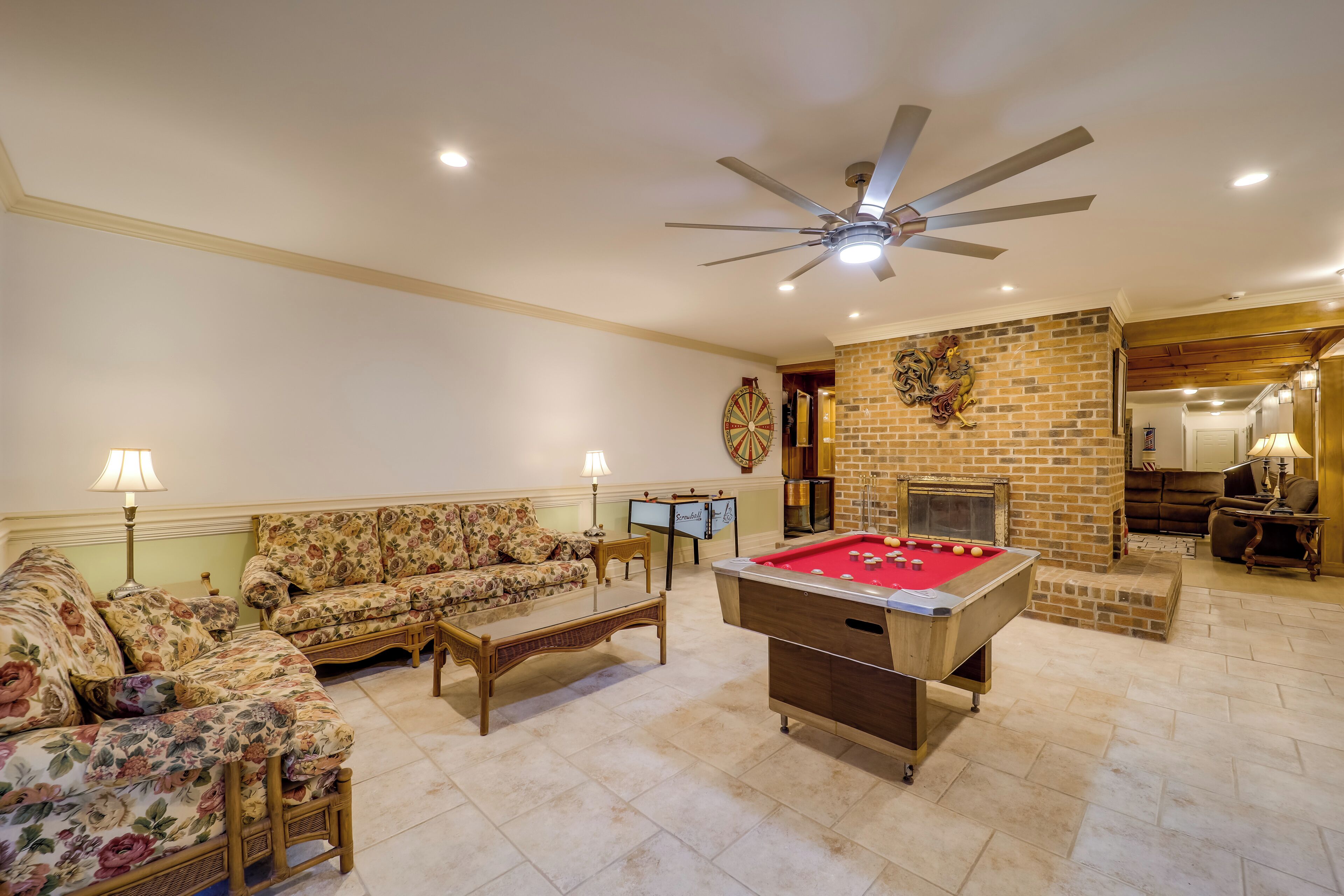A living room with a pool table, sofas, a fireplace, and a ceiling fan.