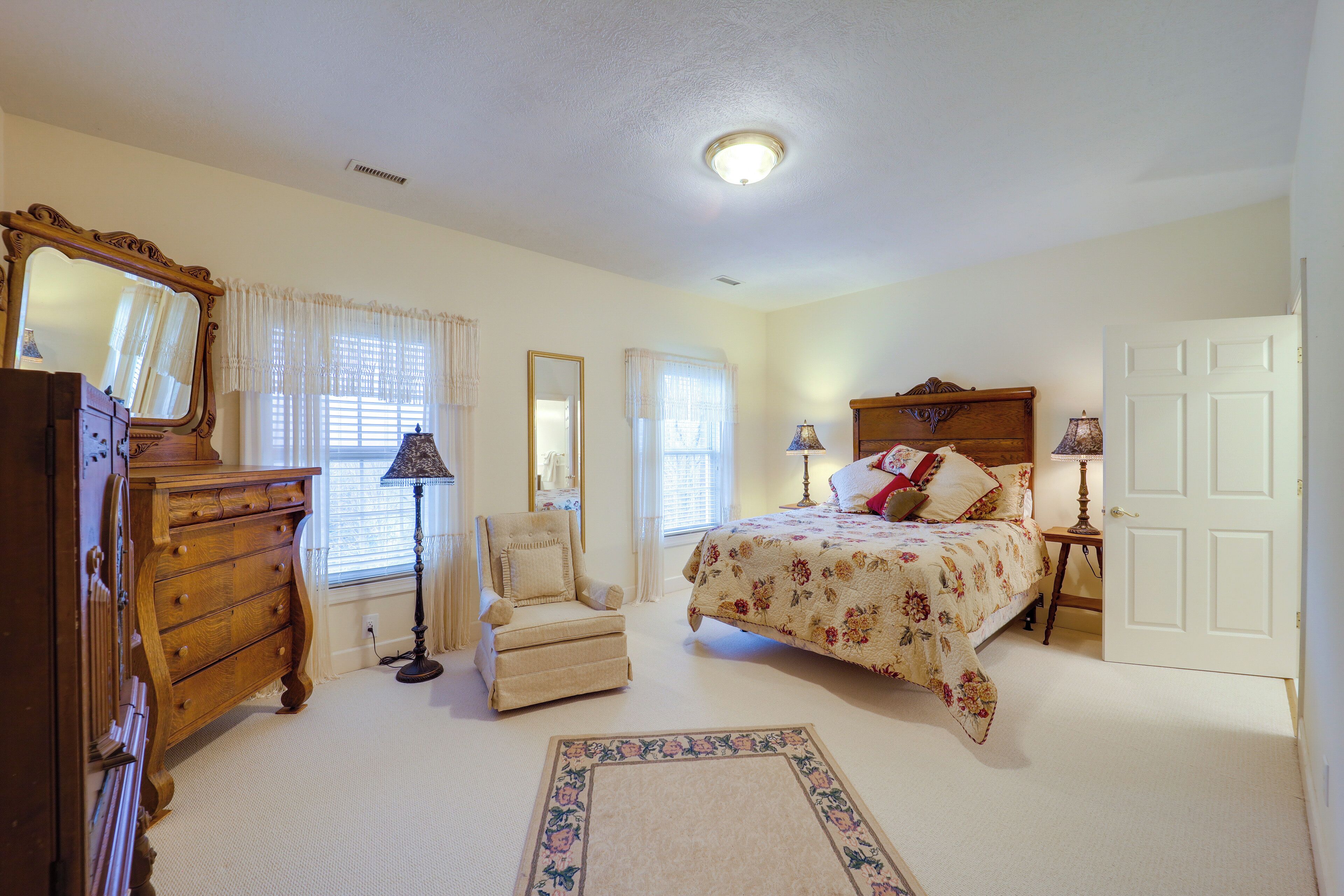 A bedroom with a bed, dresser, chair, and a large mirror.