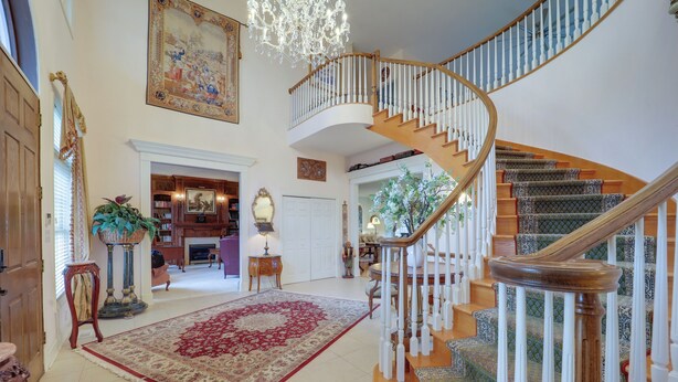 A spacious foyer with a grand staircase, a large chandelier, and a red patterned rug. - Immaculate Boone Villa w/ Entertainment Lounge! (Boone)