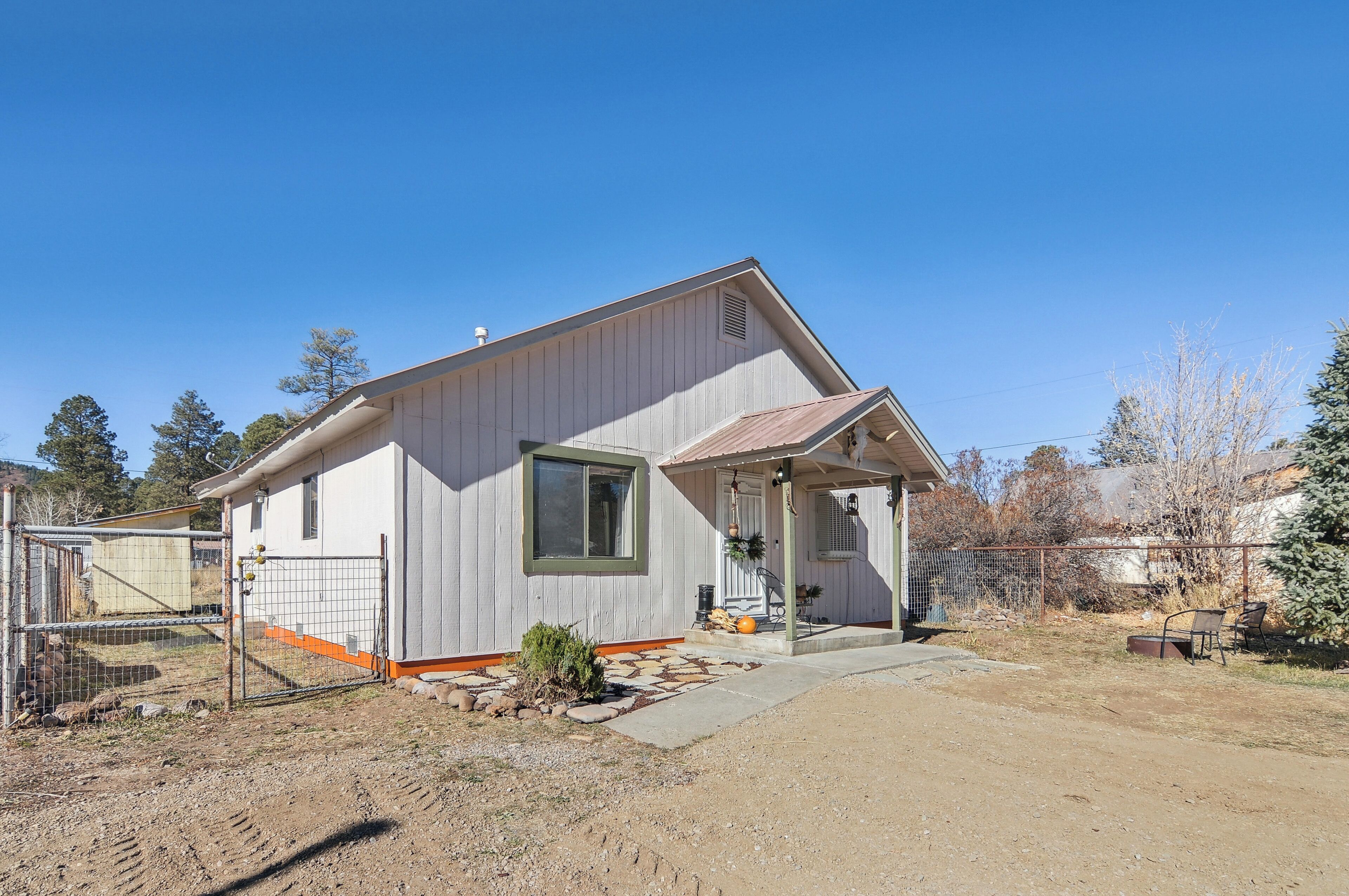 A single-story house with a covered porch, a fenced yard, and a clear blue sky.