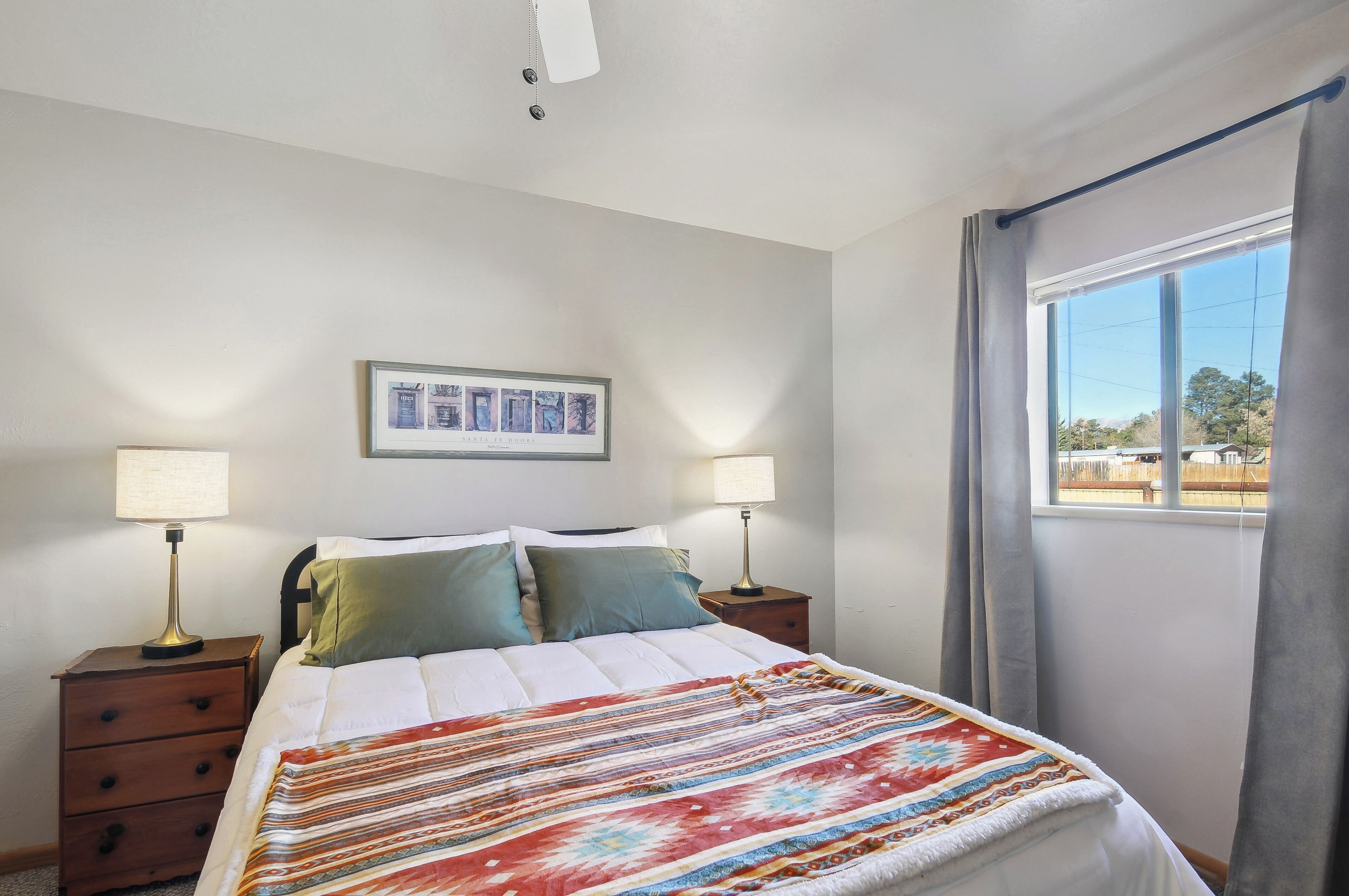 Un dormitorio con cama, dos mesitas de noche con lámparas, un cuadro en la pared y una ventana con cortinas.