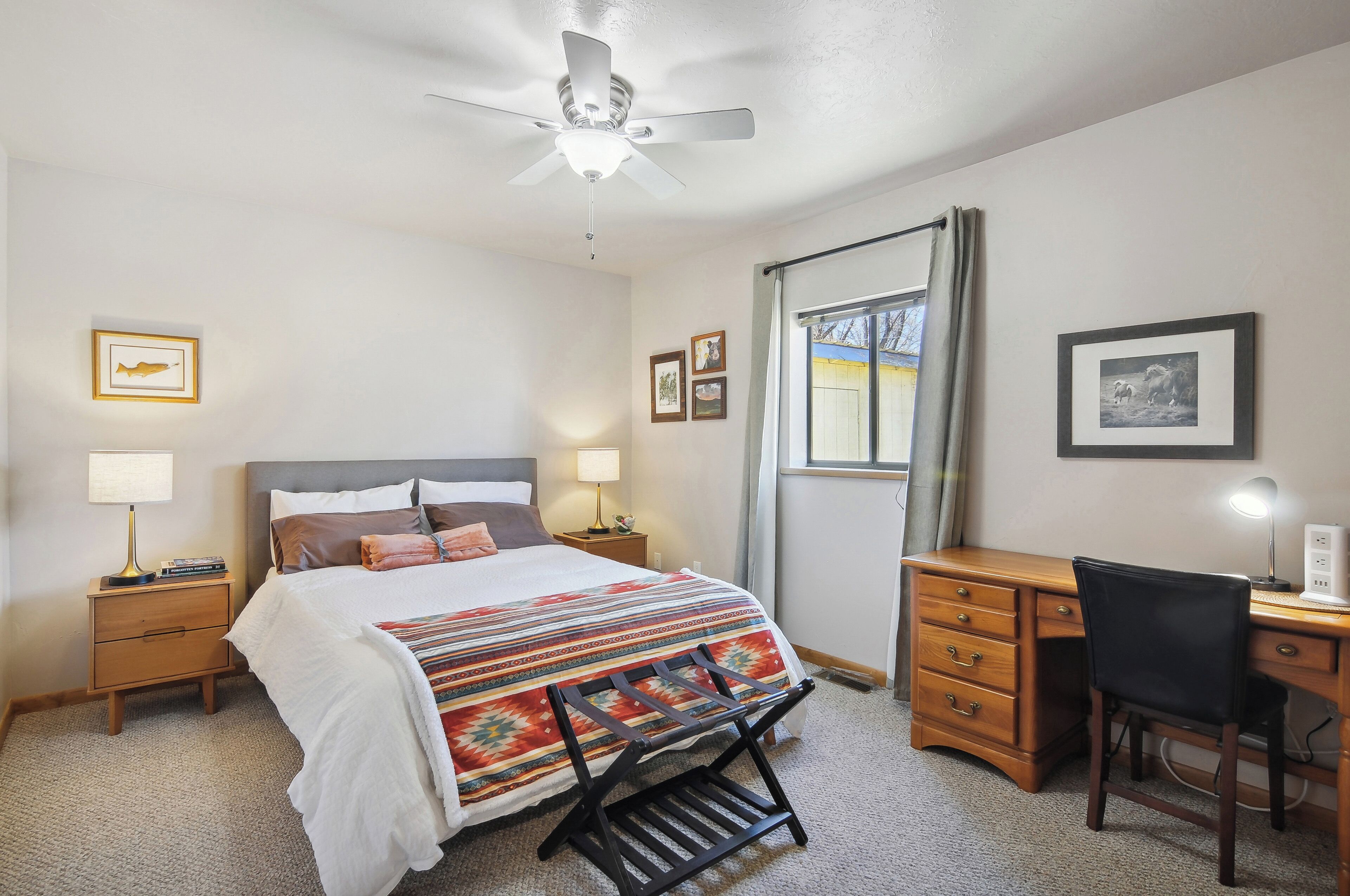 A bedroom with a bed, bedside tables, a desk, a chair, and a ceiling fan.