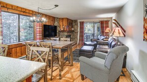 A cozy cabin interior with a dining area, a fireplace, a living room with a sofa and a lamp, and large windows offering a view of the outdoors. - Condo w/ Pool Access: 2 Mi to Winter Park Resort! (Winter Park)