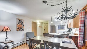 A dining area with a wooden table and chairs, a chandelier, and a kitchen in the background. - Condo w/ Pool Access: 2 Mi to Winter Park Resort! (Winter Park)