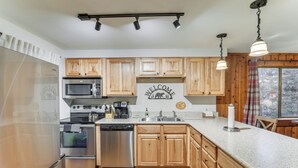 A modern kitchen with wooden cabinets, stainless steel appliances, a welcome sign, and a large window. - Condo w/ Pool Access: 2 Mi to Winter Park Resort! (Winter Park)