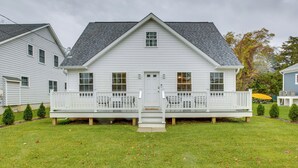 Une maison blanche à deux étages, dotée d’un porche à l’avant, d’un petit jardin et d’un toit gris.
