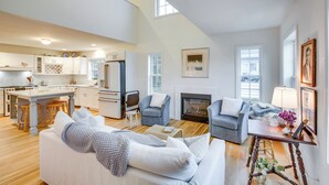 Un vaste salon avec un canapé blanc, une cheminée et une cuisine à l’arrière-plan.