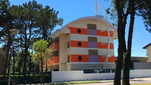 A modern building with a unique geometric facade, surrounded by trees and a clear sky.