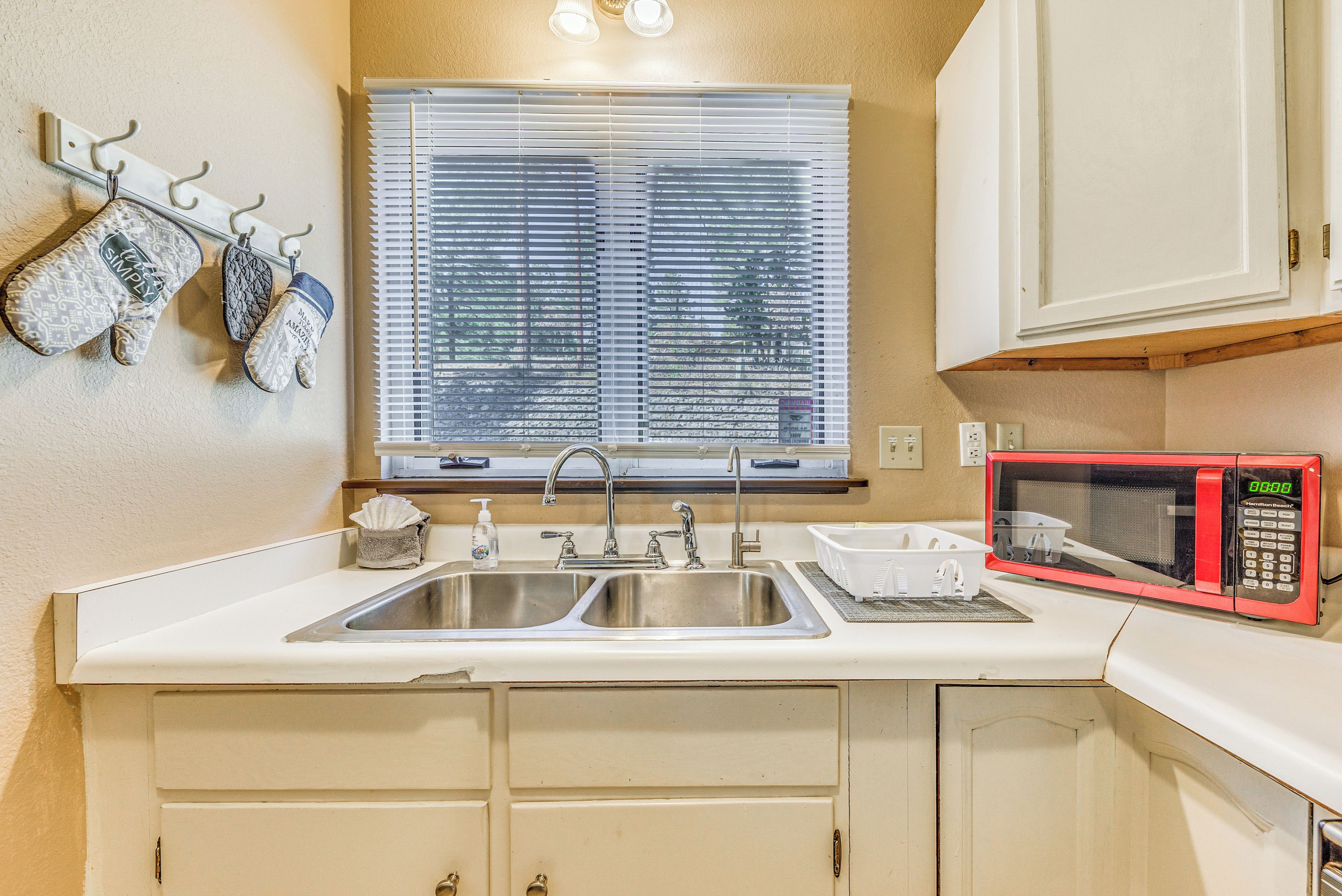 A kitchen with a double sink, a microwave, and a window with blinds.