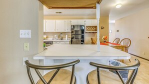 A modern kitchen with white cabinets, a central island with bar stools, and a dining area with wooden chairs. - Ruidoso Retreat w/ Grill ~ 3 Mi to Grindstone Lake (Ruidoso)