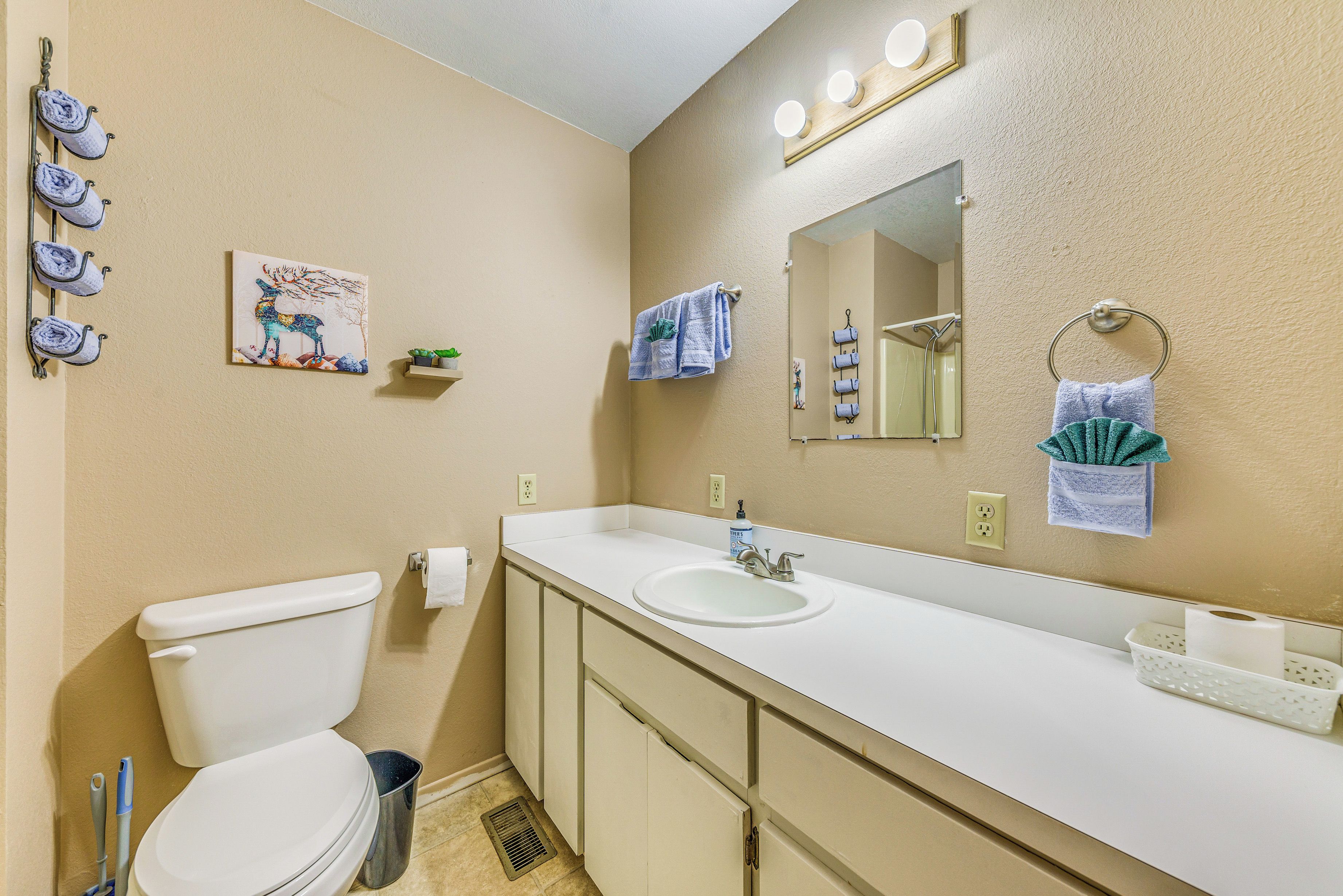 A bathroom with a toilet, sink, and mirror. There are towels hanging on the wall and a painting above the sink.