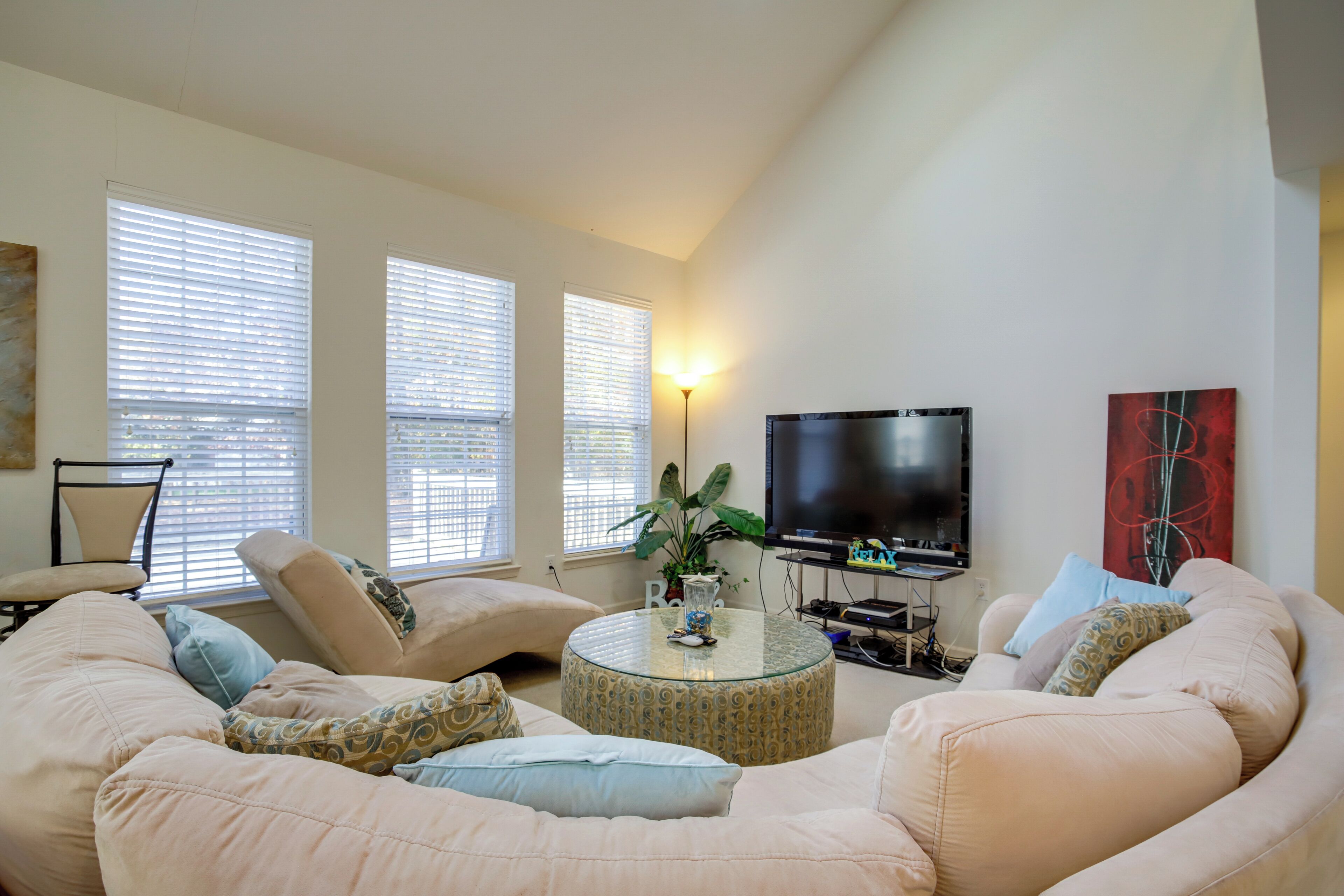 Una sala de estar con un sofá beige grande, una mesa de centro de vidrio, un televisor y una planta.