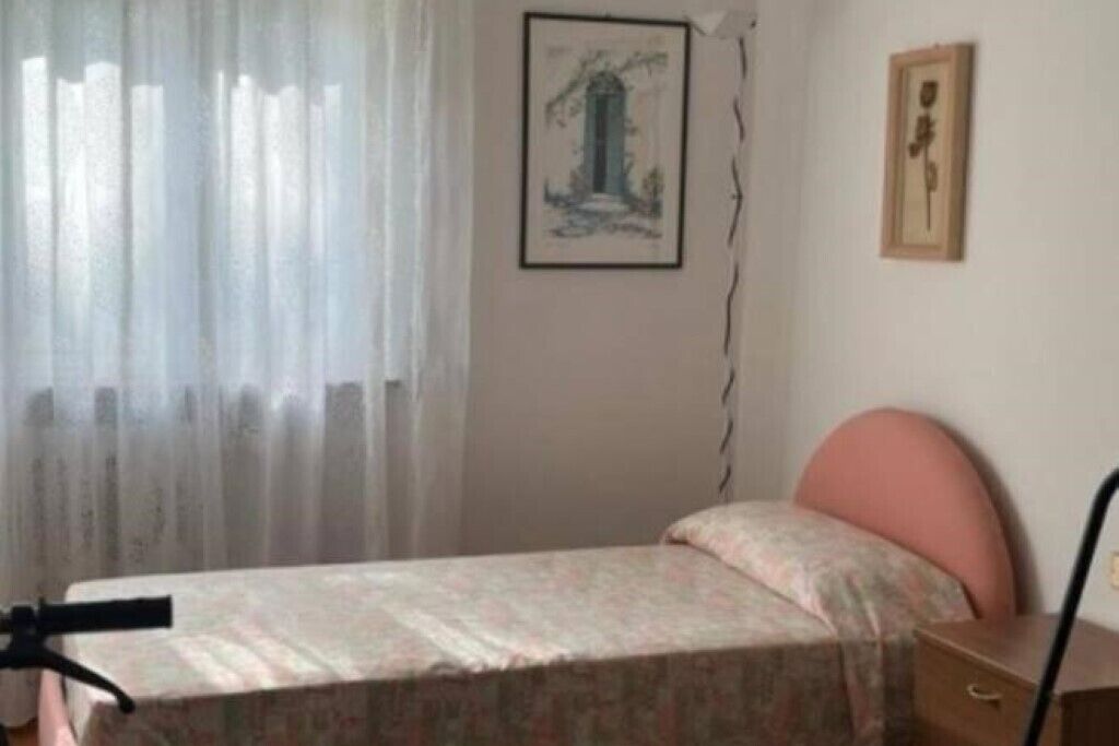 Una cama individual con colcha estampada, una mesita de noche y una silla.