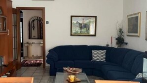 A living room with a dark blue sofa, a coffee table with a bowl and flowers, a framed painting on the wall, and an air conditioning unit above the sofa.