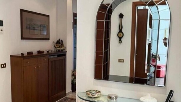 A hallway with a wooden cabinet, a framed picture on the wall, and a glass table with a phone and a bowl.