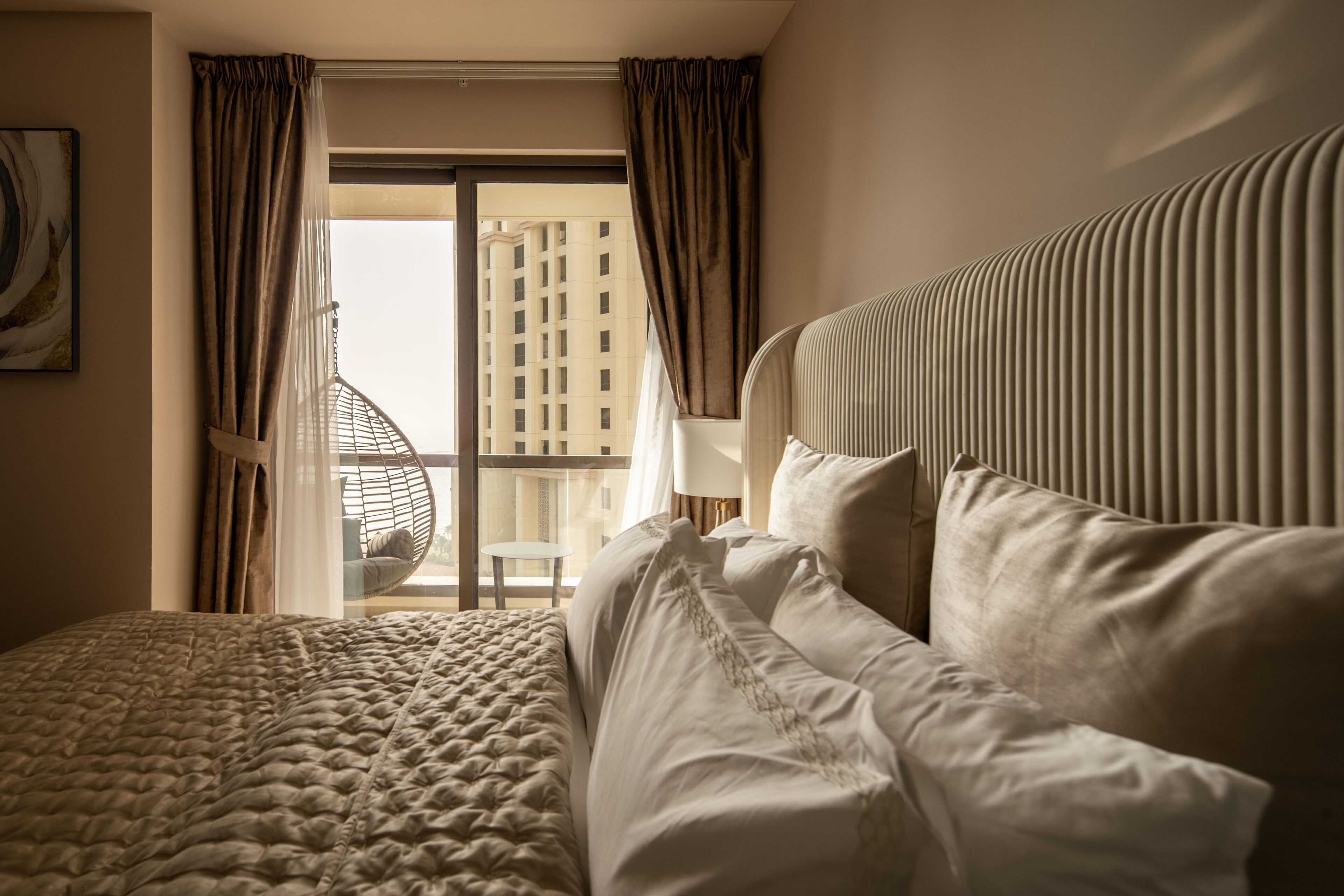 Une chambre d’hôtel avec un grand lit, une vue sur le paysage urbain par la fenêtre et un fauteuil suspendu près de la fenêtre.