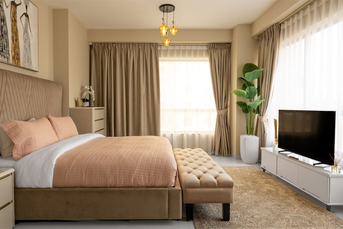 A modern bedroom with a large bed, a TV, and a plant.
