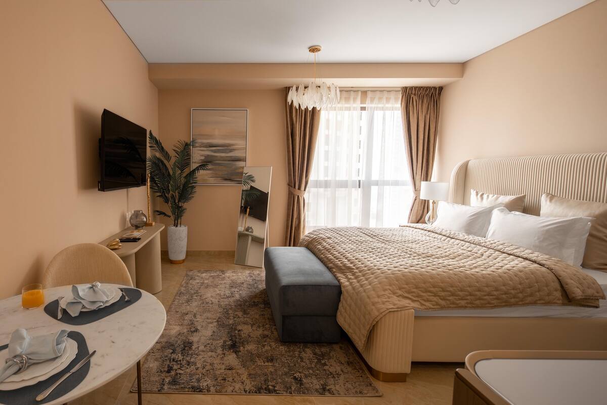A modern hotel room with a bed, a desk, a chair, a small table, and a TV.