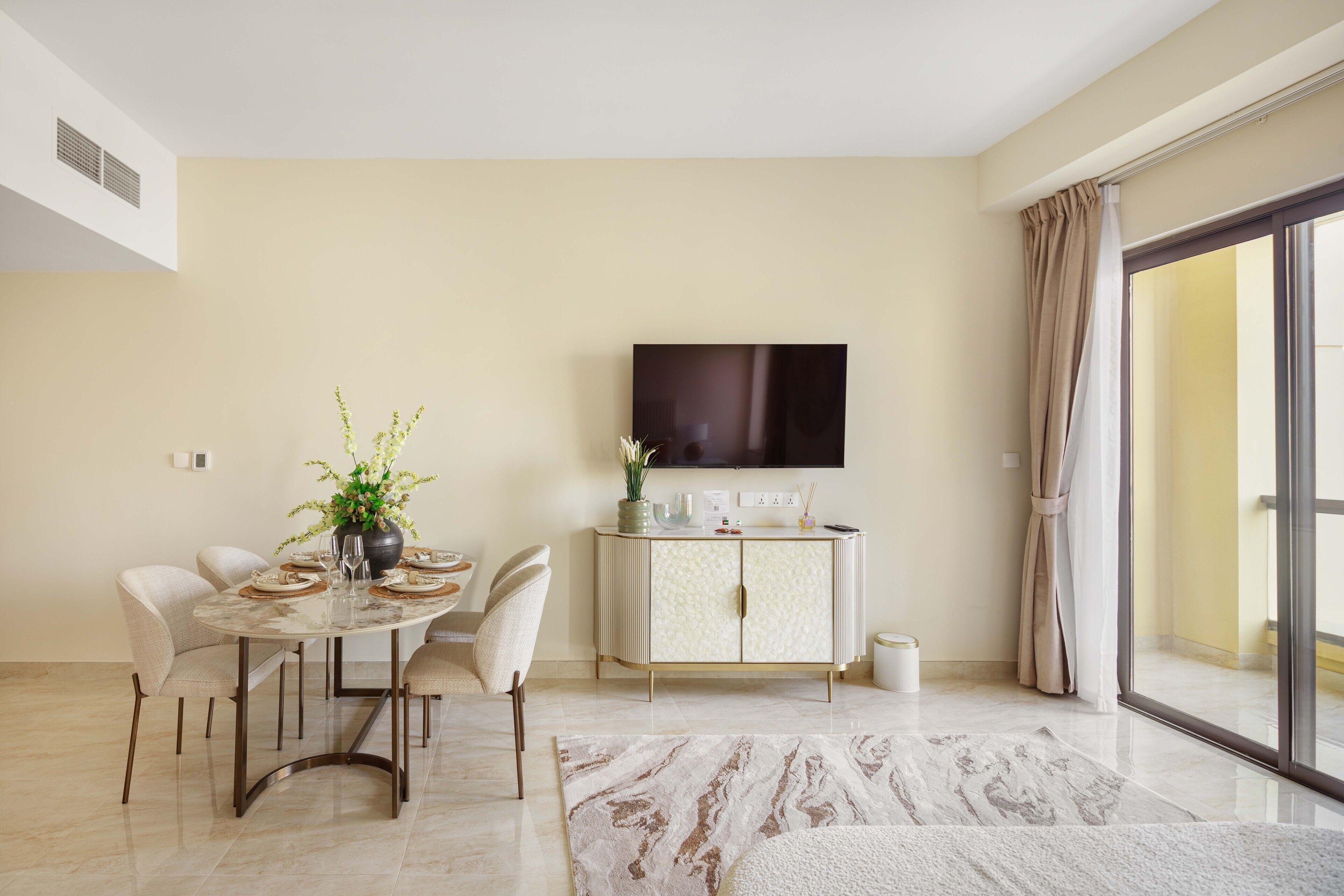 A modern dining area with a round table, chairs, a cabinet, and a flat-screen TV on the wall.