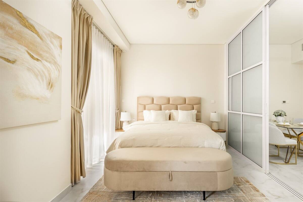 A modern bedroom with a large bed, a headboard, bedside tables, and a view through a glass door.
