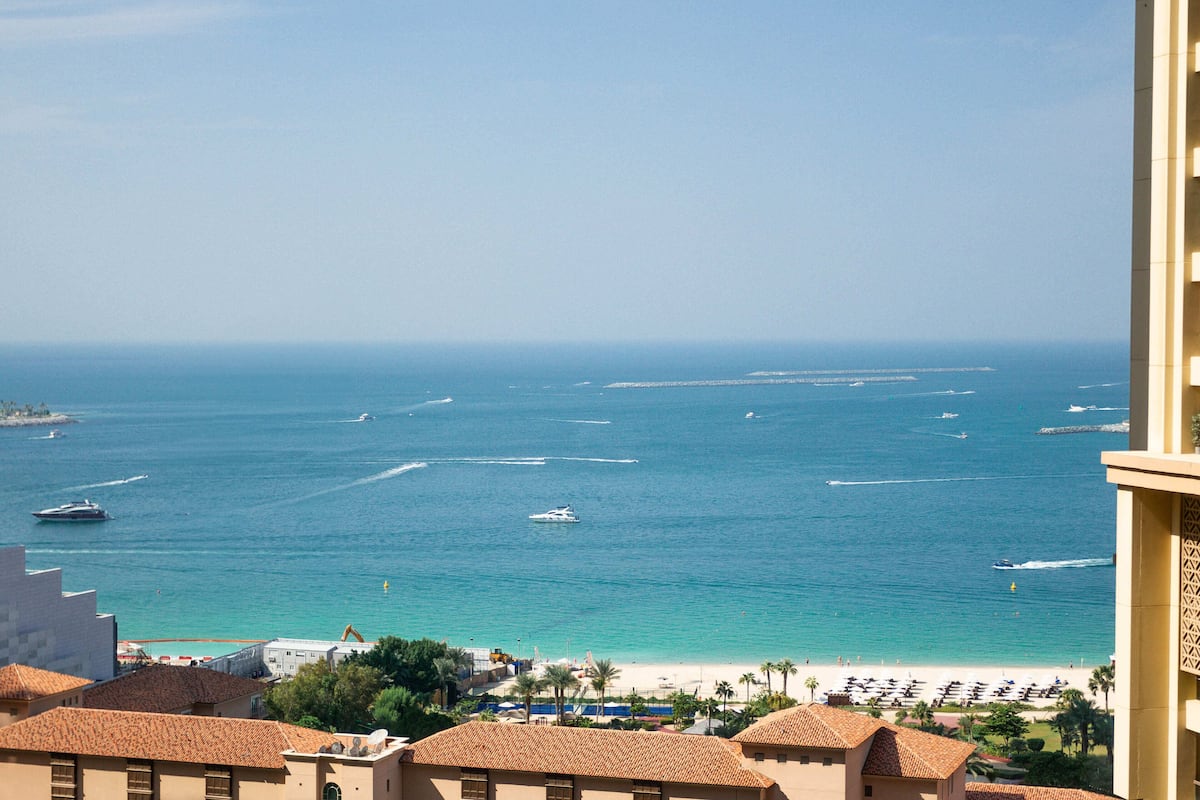 A coastal view with a beach, boats, and buildings with tiled roofs.