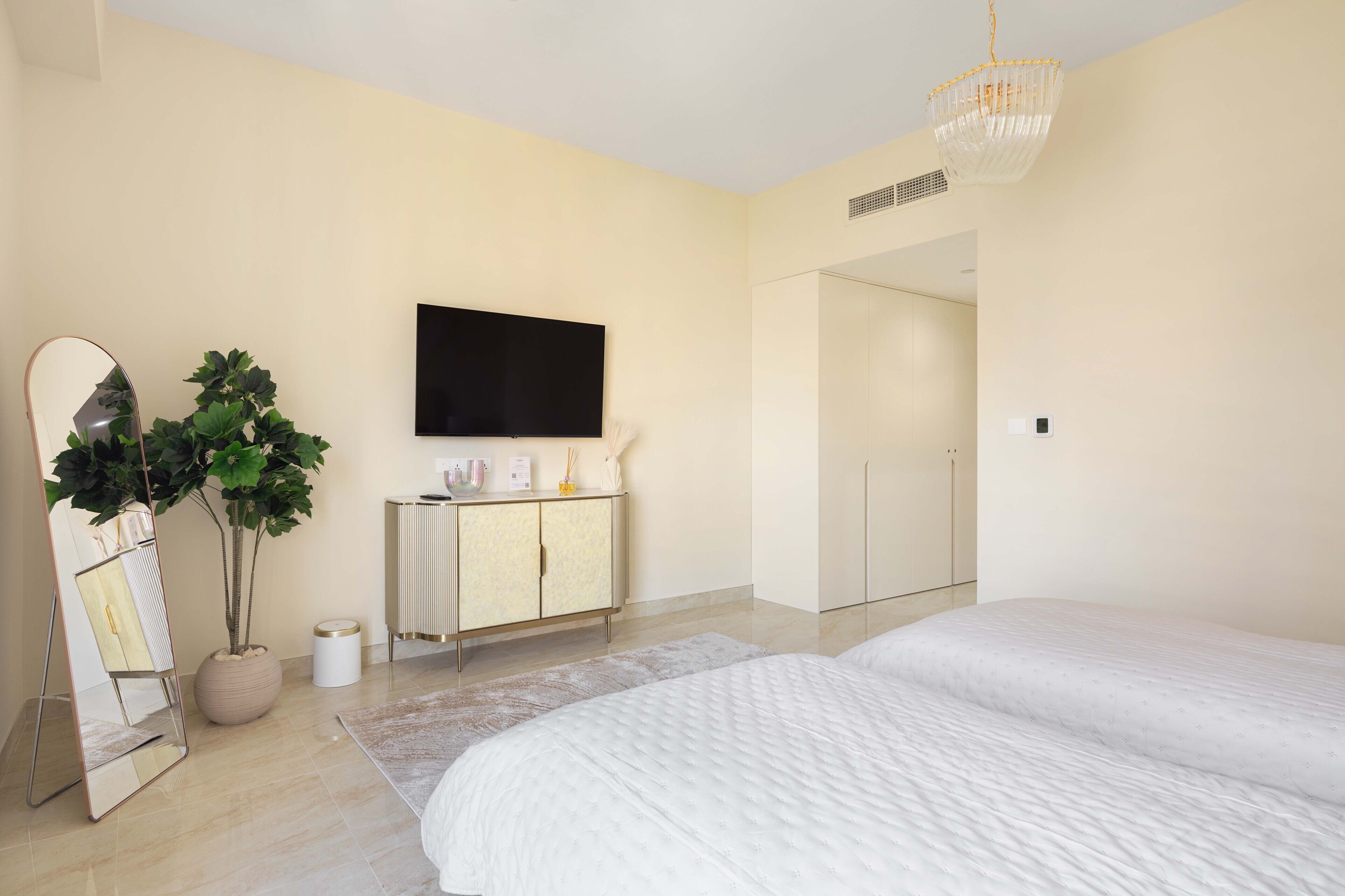 Un dormitorio moderno con dos camas, un espejo grande, una planta en maceta, un televisor de pantalla plana y un aparador minimalista.
