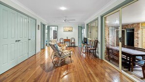 Una habitación amplia con piso de madera, un comedor con mesa y sillas de madera, un televisor y un ventilador de techo.