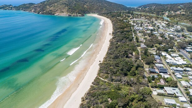 Vista aérea de una zona costera con playa, edificios residenciales y un paisaje montañoso.