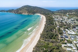 An aerial view of a coastal area with a beach, residential buildings, and a hilly landscape.