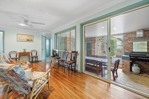 A spacious living area with wooden flooring, a ceiling fan, and a brick fireplace.