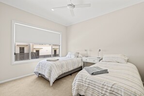 Ein Schlafzimmer mit zwei Betten, einem Fenster, einem Deckenventilator und einem Nachttisch.