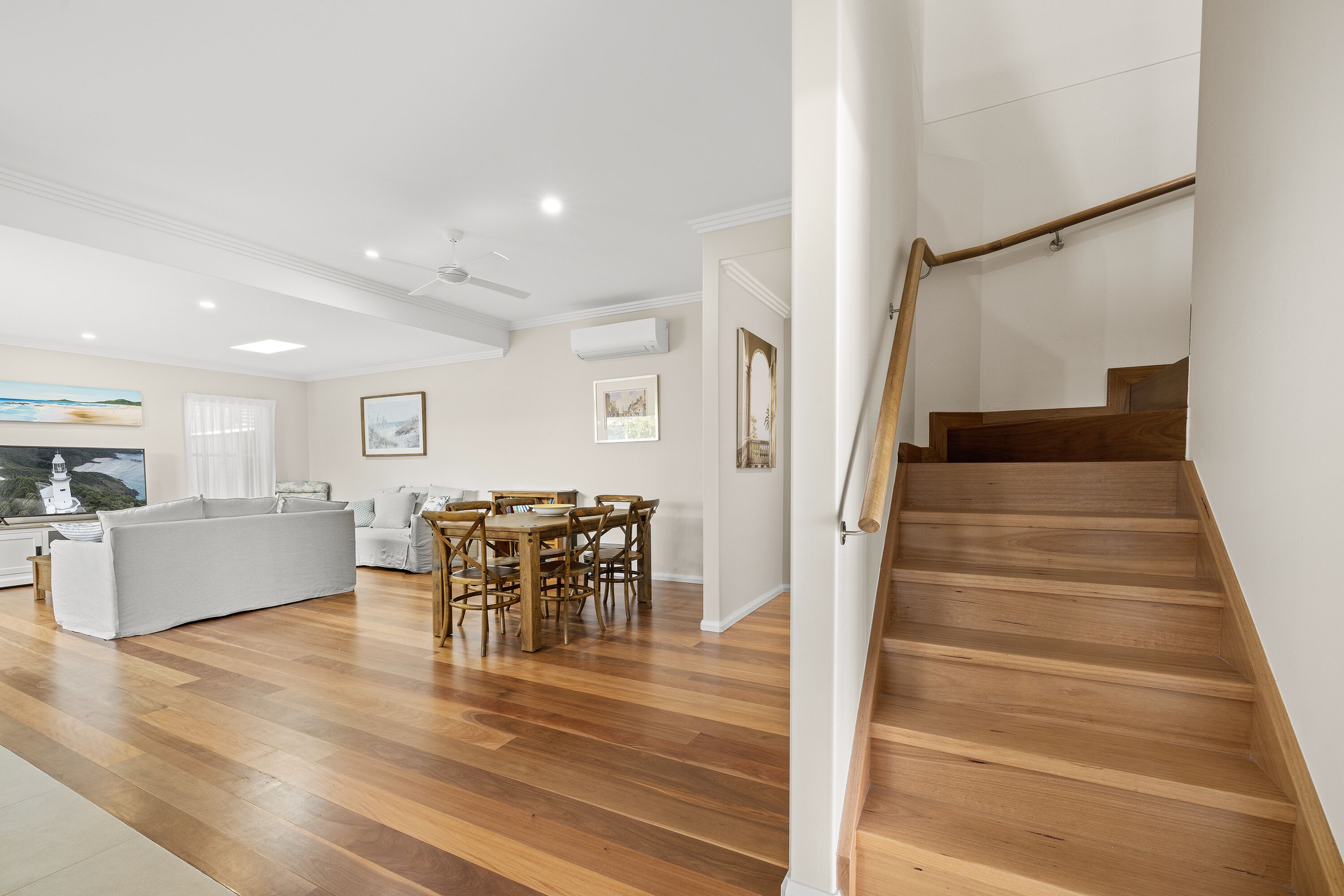A spacious living area with a wooden staircase, a dining table, and a sofa.