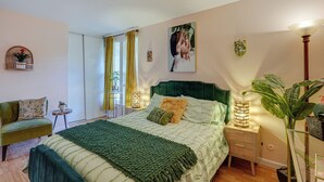 Ein Schlafzimmer mit Bett, Nachttischen, einem Sessel, einem Fenster mit Vorhängen und einer Pflanze.