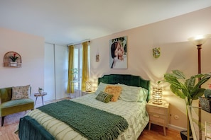 Une chambre à coucher avec un lit, des tables de chevet, une chaise, une fenêtre avec des rideaux et une plante.