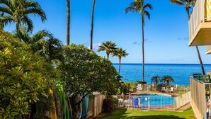 A pool area with a view of the ocean, surrounded by palm trees and a clear blue sky. - Oceanfront Kihei Condo With On-site Beach Access! (Kihei)