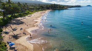 A beach with clear water, people swimming and sunbathing, and a view of the ocean and distant hills. - Oceanfront Kihei Condo With On-site Beach Access! (Kihei)