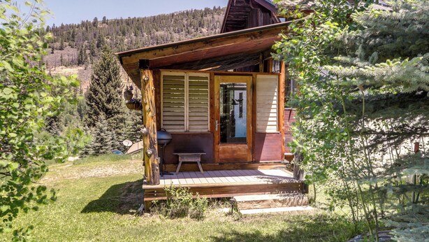 Une cabane rustique avec une façade en bois, une véranda et une porte donnant sur l’intérieur.