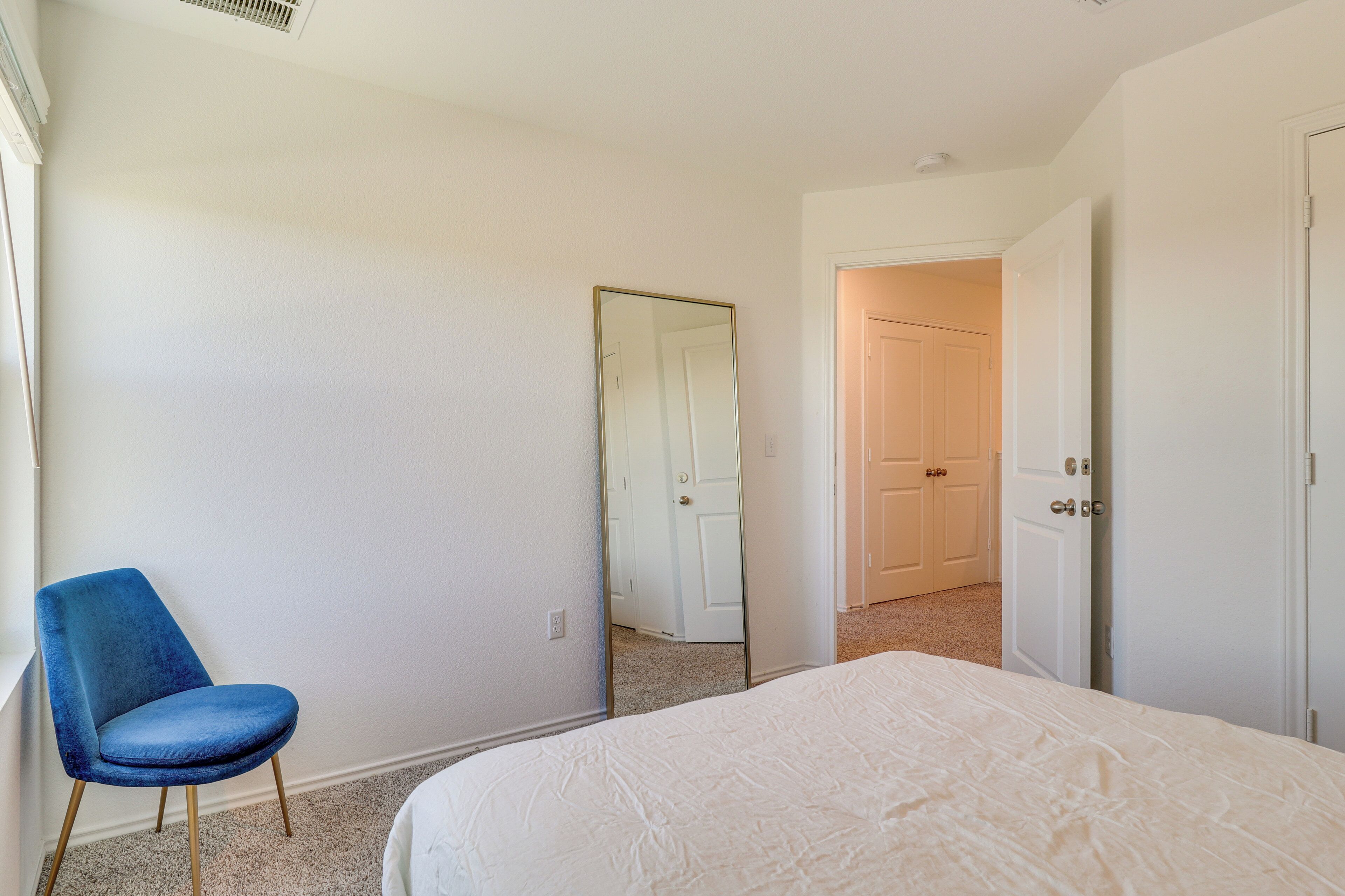 A bedroom with a bed, a blue chair, and a door leading to another room.