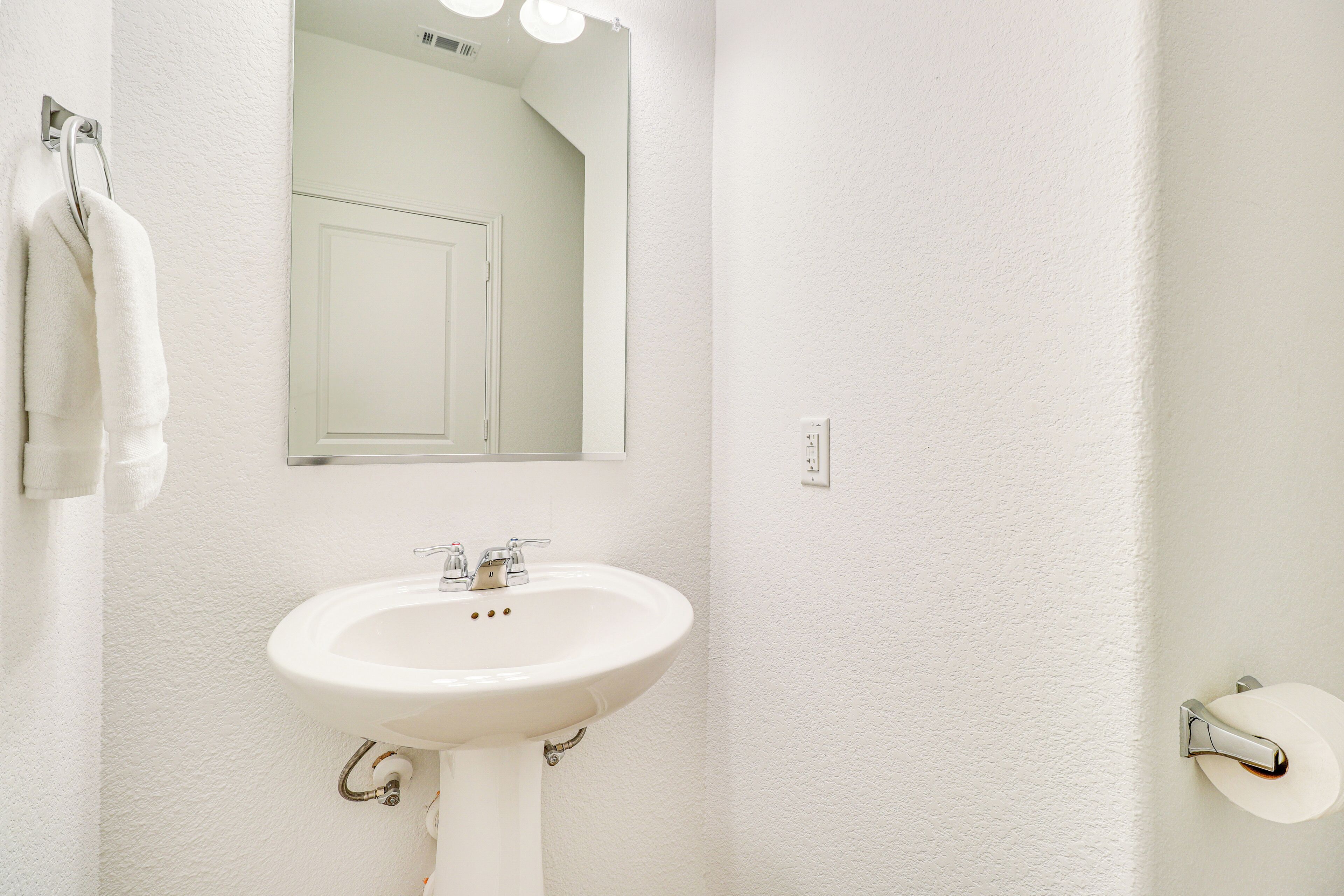 A white bathroom with a sink, mirror, towel rack, and toilet paper holder.
